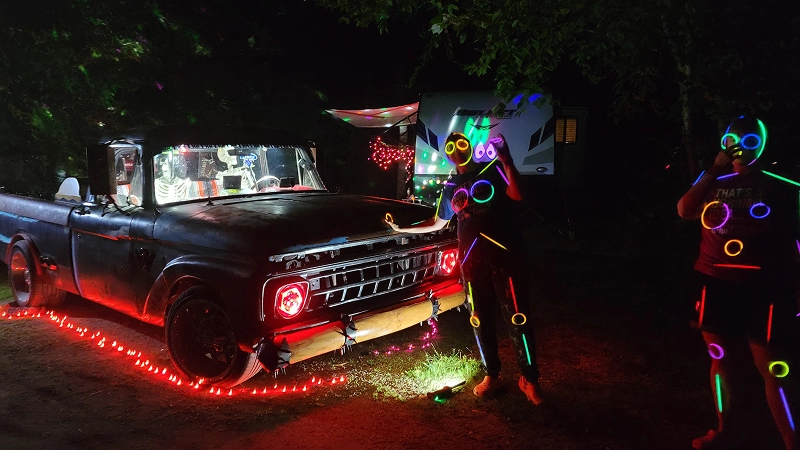 Glowing figures beside illuminated vintage truck.