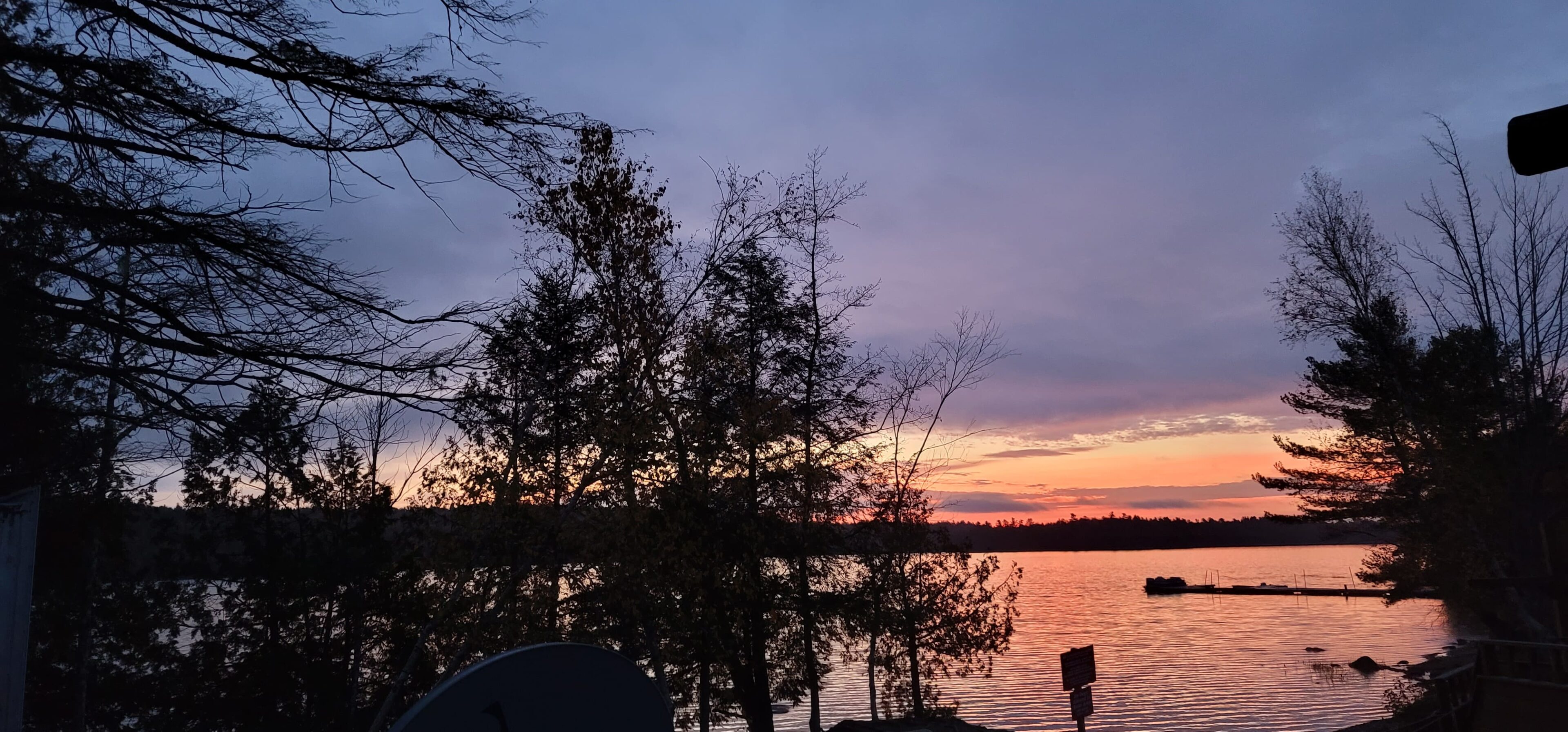 A sunset over the water with trees in front of it.