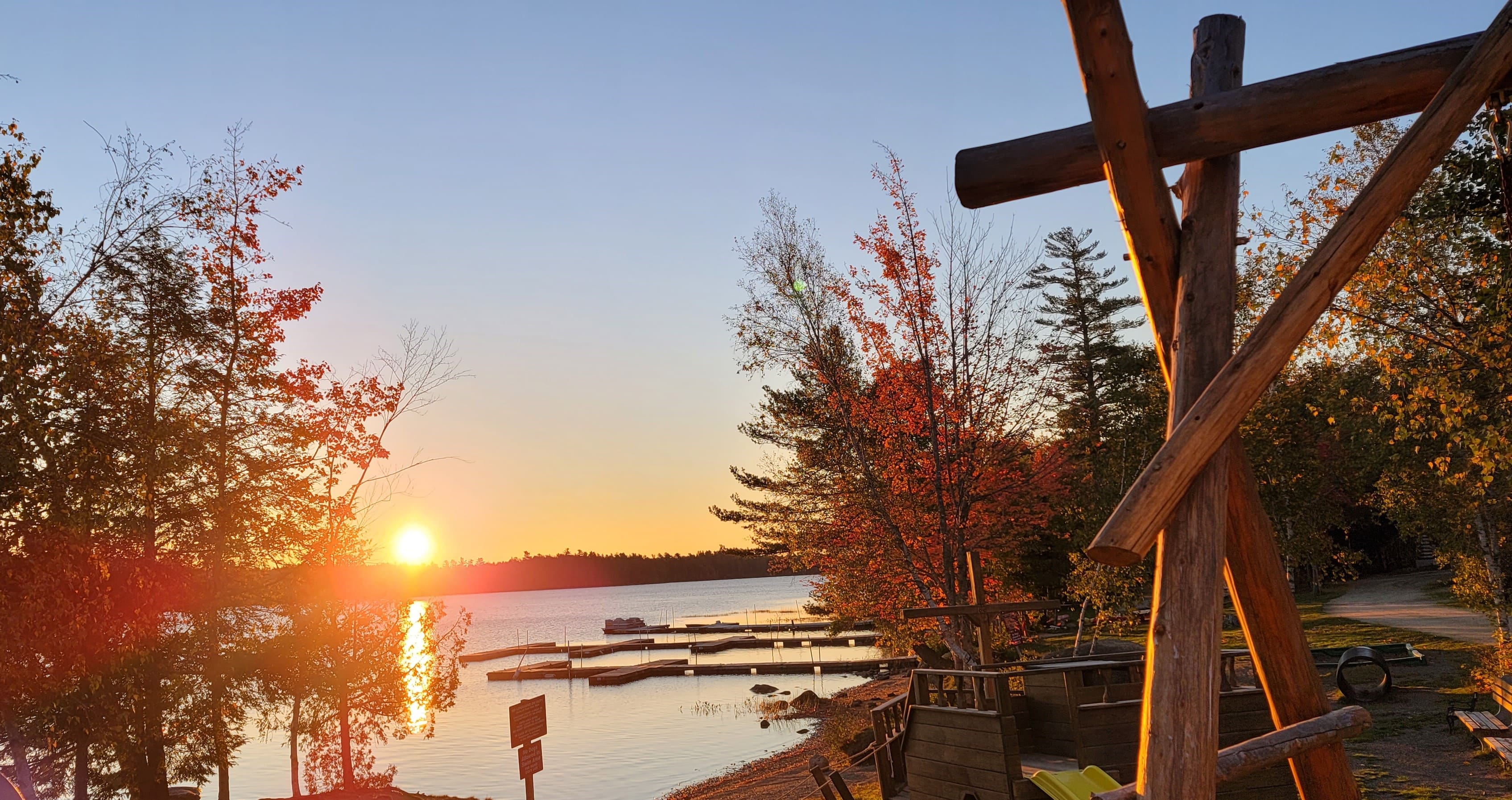 A sunset over the water with trees and benches.