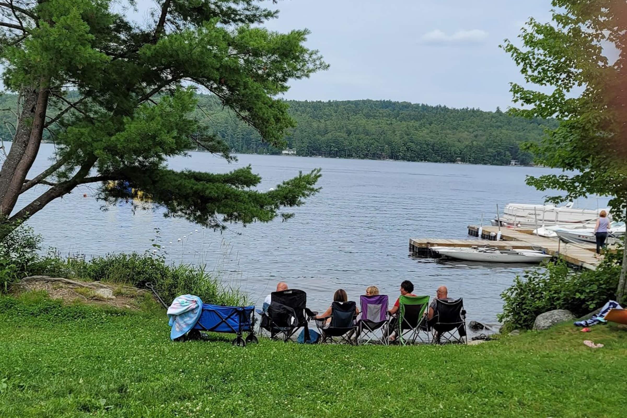 A group of people sitting on the grass near water.