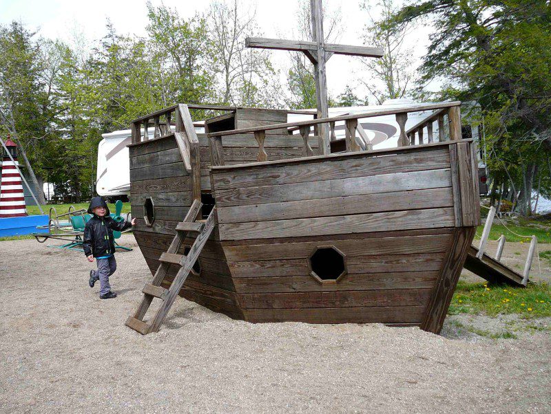 New Project (9) A child is standing next to a wooden boat.